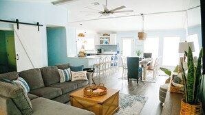 A spacious living room with a sofa, coffee table, and a dining area with chairs and a table. - Beachside Family Getaway Nestled in the Woods at Fort Morgan, AL (Gulf Shores)