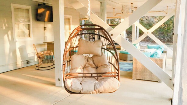 A hanging chair with cushions, a wicker chair, and a sofa with cushions in a covered outdoor area with a view of the outdoors. - Beachside Family Getaway Nestled in the Woods at Fort Morgan, AL (Gulf Shores)