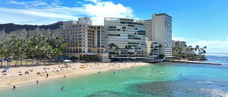 Un hotel frente a la playa con varios pisos, una playa de arena y palmeras.