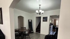 Un comedor espacioso con una mesa y sillas de madera, una escalera que sube a un nivel superior y un candelabro.