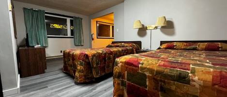 A hotel room with two beds, a wooden nightstand, a lamp, and a window with curtains.
