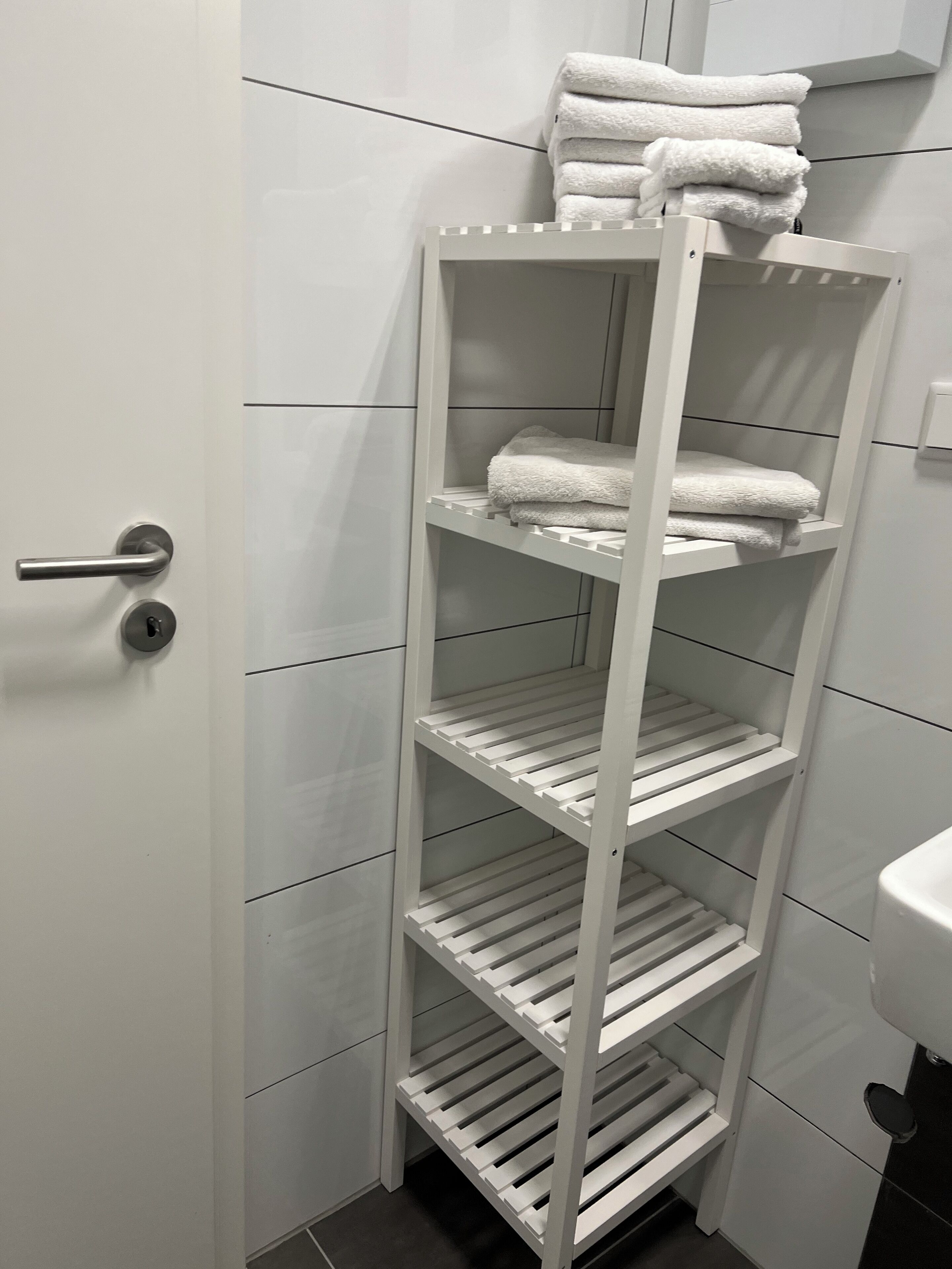 En vit hylla i metall med handdukar, placerad i ett badrum.