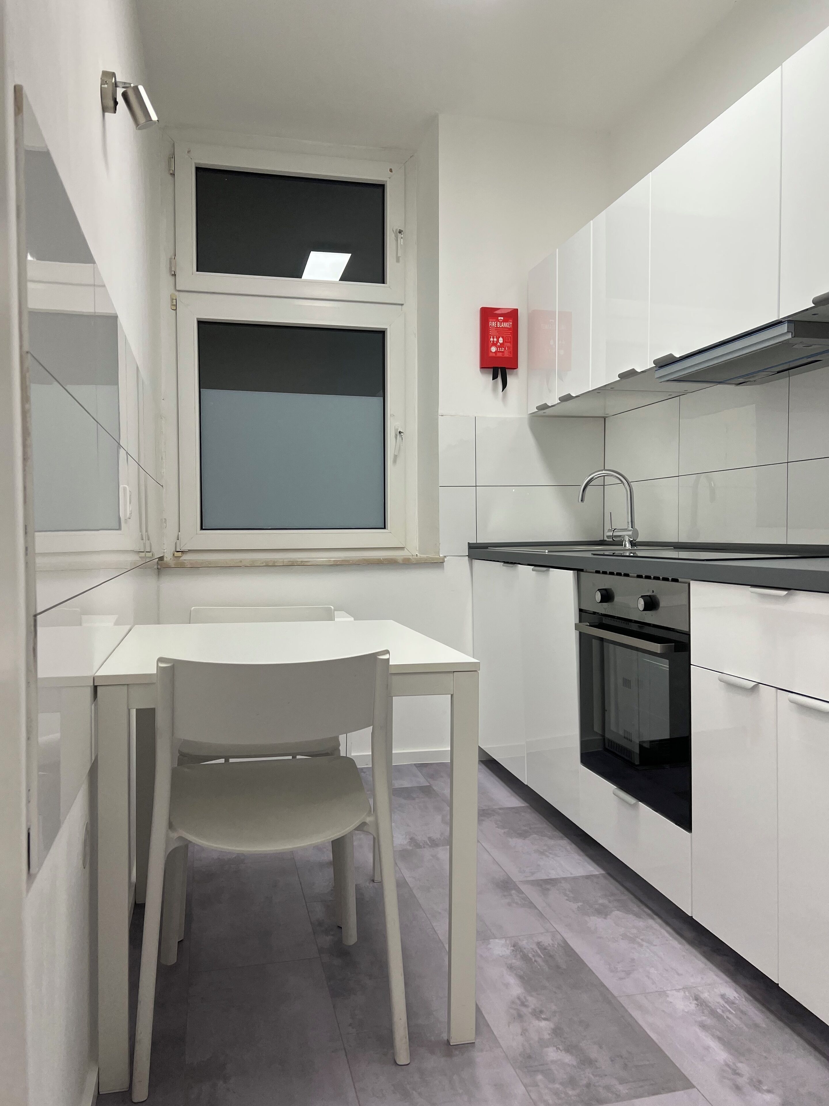 Eine kleine Küche mit weißen Schränken, einem eingebauten Backofen und einem Fenster über der Spüle.