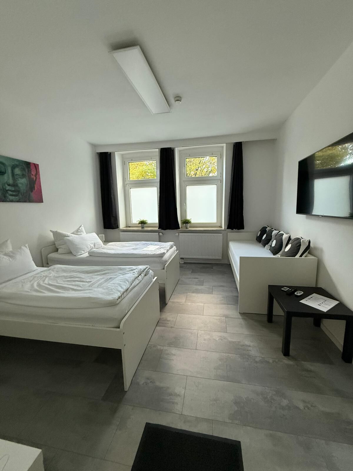Een moderne hotelkamer met twee bedden, een bank, een televisie en een raam met gordijnen.