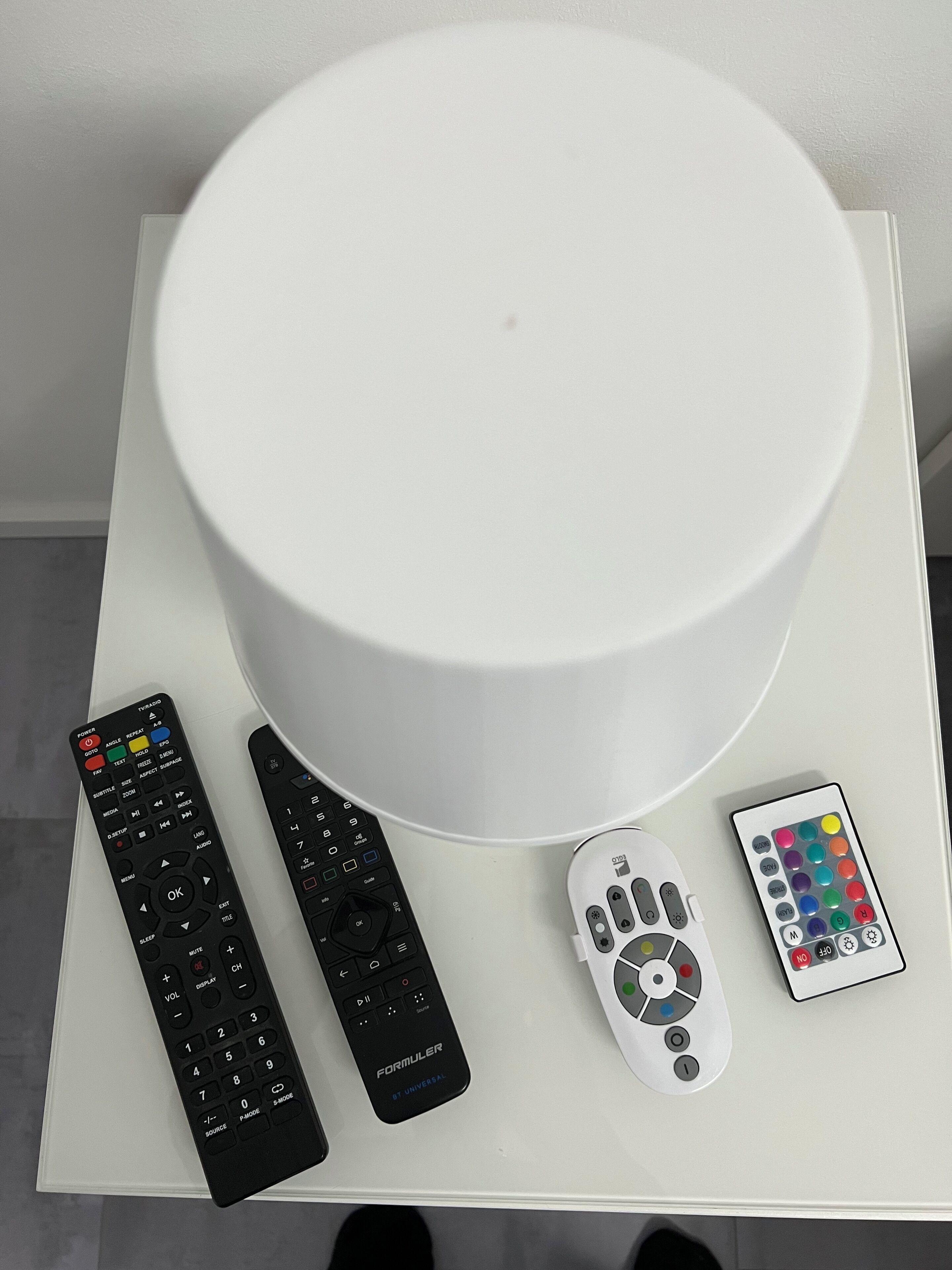 Une table blanche avec quatre télécommandes et un objet cylindrique blanc.