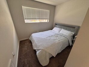 A small, neatly arranged bedroom with a single bed, a window with blinds, and a carpeted floor. - Charming 2-bedroom bungalow in welcoming Burien (Burien)