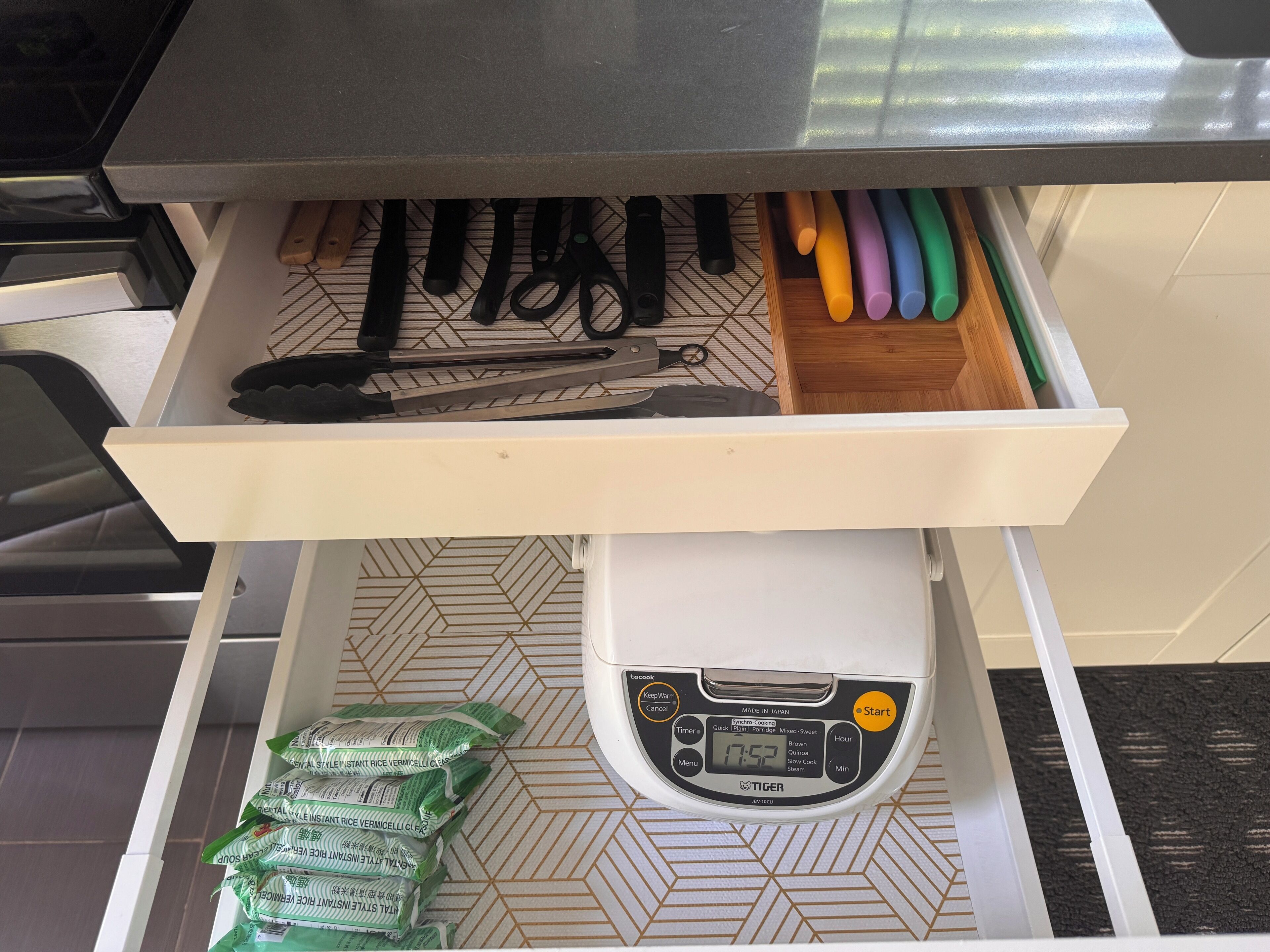 A kitchen drawer with various utensils, a rice cooker, and packets of rice.