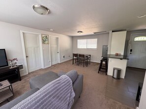 A living room with a grey sofa, a dining table with four chairs, a TV on a stand, and a small trash can. - Charming 2-bedroom bungalow in welcoming Burien (Burien)