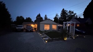 Une allée menant à une résidence, avec deux voitures garées, une pelouse bien entretenue et une porte blanche.