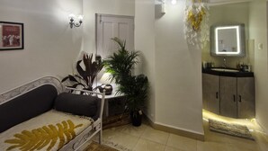 A modern living room with a sofa, coffee table, and potted plants. A door leads to a bathroom with a sink and mirror. - Janki's hideout
Nature & Peaceful vibe – for people seeking relaxation and calm. (Palolem, south goa)