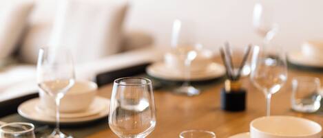 A dining table set with white plates, bowls, and wine glasses, with a painting on the wall behind.