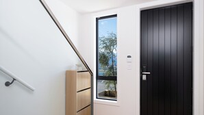 Un intérieur moderne avec un escalier, une porte noire et une fenêtre donnant sur des arbres.