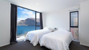 Une chambre avec deux lits, une grande fenêtre donnant sur un paysage montagneux et un balcon avec un mur en pierre.