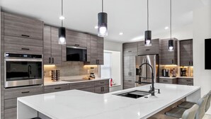 A modern kitchen with a large island, stainless steel appliances, and pendant lighting. - Staycation Station (Tampa)