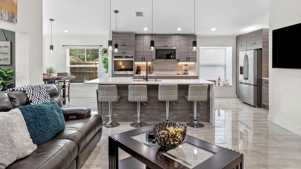 A modern kitchen with a central island, bar stools, and a dining area with a glass table. - Staycation Station (Tampa)
