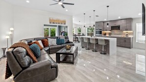 A modern living room with a leather sofa, a coffee table, and a dining area with bar stools. - Staycation Station (Tampa)