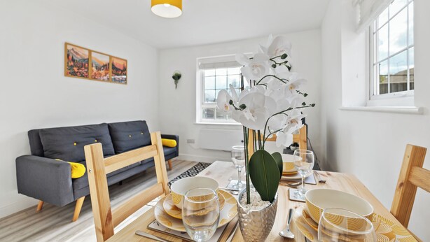 A modern living room with a dining area, featuring a sofa, dining table, and orchid plant. - 4 Min to LTN | Modern Stylish | WiFi | FreeParking (Luton)