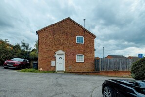 Un petit bâtiment en briques avec une porte et des fenêtres blanches, une voiture garée devant et une clôture en arrière-plan.
