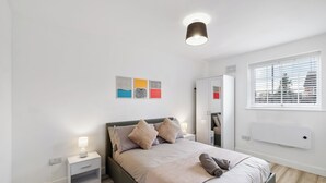 A modern bedroom with a bed, bedside tables, a mirror, and artwork on the wall. - 4 Min to LTN | Modern Stylish | WiFi | FreeParking (Luton)