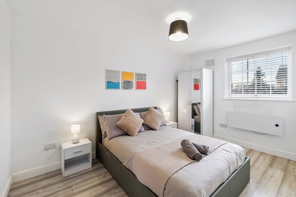 Une chambre à coucher moderne avec un lit, des tables de chevet, un miroir et des œuvres d’art accrochées au mur.