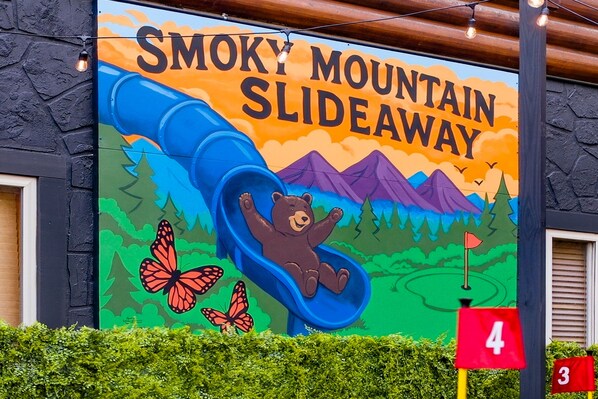 A mural of a bear sliding down a mountain slide with butterflies and a golf flag.