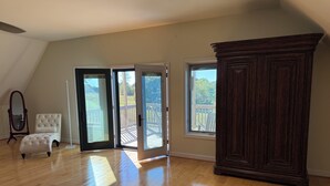 A spacious room with wooden flooring, a large dark wooden cabinet, a white upholstered chair, and a full-length mirror. - Charming 2-bedroom barndominium in historic Appomattox Virginia. (Appomattox)