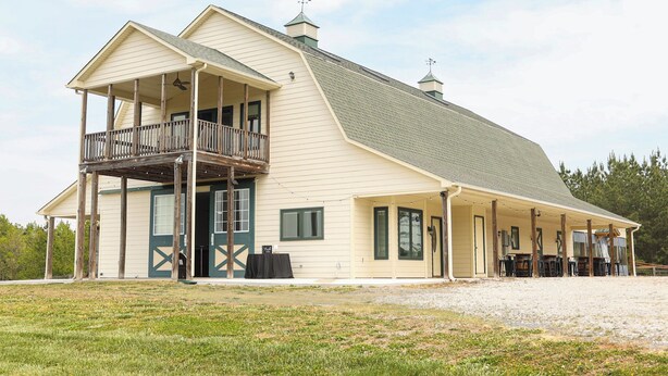 A large, single-story building with a balcony, a covered porch, and a fenced yard. - Charming 2-bedroom barndominium in historic Appomattox Virginia. (Appomattox)