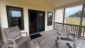 A covered porch with wooden chairs and a view of a grassy area. - Charming 2-bedroom barndominium in historic Appomattox Virginia. (Appomattox)
