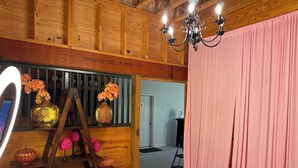 A room with wooden paneling, a chandelier, a pink curtain, and a ladder with vases of flowers. - Charming 2-bedroom barndominium in historic Appomattox Virginia. (Appomattox)