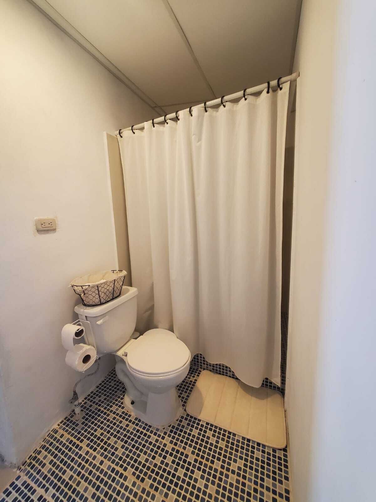 Un baño pequeño con inodoro, cortina de ducha y piso de baldosas.
