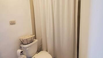 Un baño pequeño con inodoro, cortina de ducha y piso de baldosas.