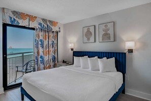 Habitación de hotel con cama, mesita de noche, lámpara, vista al océano y balcón con una silla.