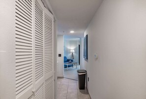 A hallway with a white door, a trash bin, a blue sofa, and a lamp in a room.