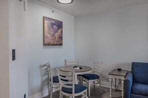 A dining area with a round table, four chairs, a painting on the wall, and a blue sofa.