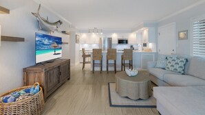 A modern living room with a TV, wicker chairs, a round coffee table, and a sofa. - BG Beach Club 3C | 3BR/2BA Boca Grande | Pool View (Boca Grande)