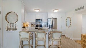 Une cuisine moderne avec des meubles blancs, des appareils en acier inoxydable et un îlot central doté de tabourets de bar.