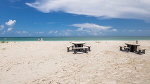 Une plage avec trois tables de pique-nique et deux chaises de plage.