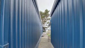 Um corredor estreito com paredes de metal azul, chão de concreto e uma bicicleta encostada na parede.