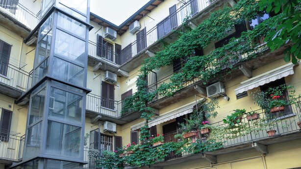 A multi-story building with balconies, air conditioning units, and potted plants. - Italianway Comfort - Rosmini 7 (Milan)