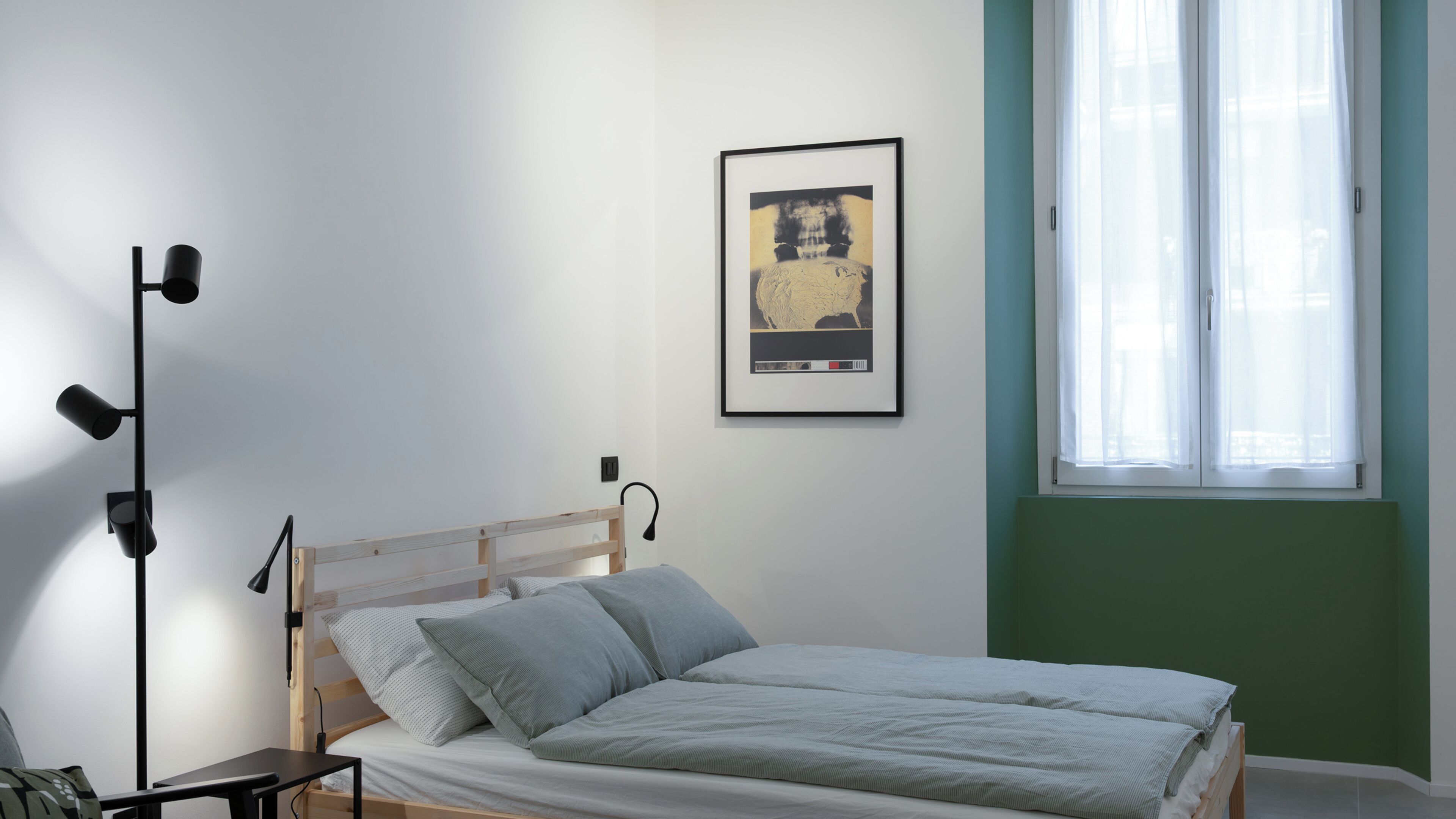 A bedroom with a bed, a bedside table, a lamp, a window, and a framed picture on the wall.