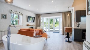 A spacious living area with a large white bathtub, orange seating, a kitchen area, and a sliding glass door leading to a garden. - The Pig Sty - 1 Bedroom Studio - Princes Gate (Narberth)