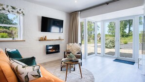 A modern living room with a fireplace, a flat-screen TV, and a large sliding glass door leading to an outdoor area. - The Pig Sty - 1 Bedroom Studio - Princes Gate (Narberth)