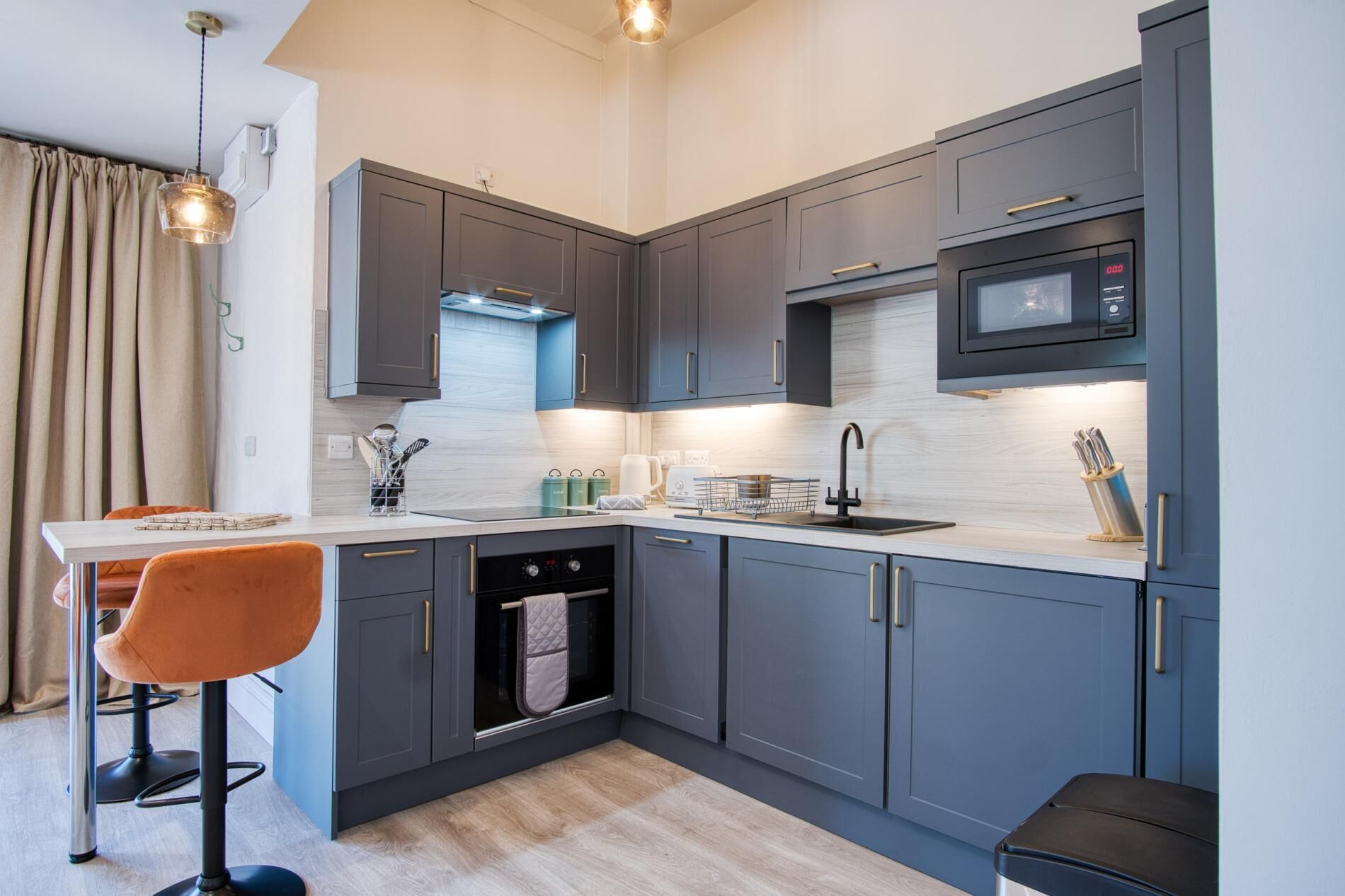 A modern kitchen with grey cabinets, a built-in microwave, and a stainless steel sink.
