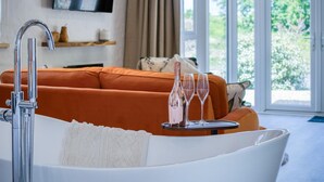 A modern bathroom with a bathtub, a shower, and a sink. There is a window with a view of greenery outside. - The Pig Sty - 1 Bedroom Studio - Princes Gate (Narberth)