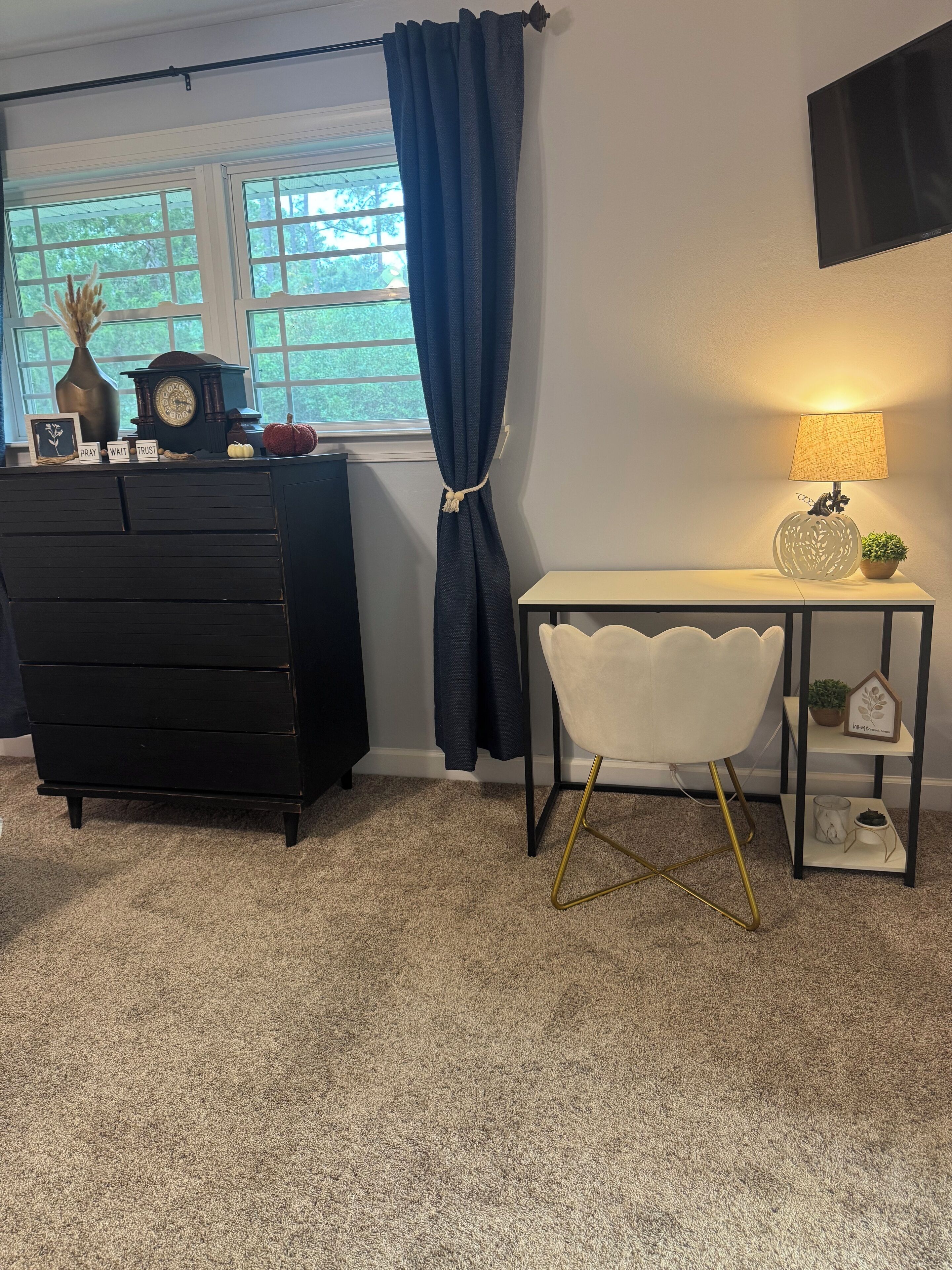 A room with a dresser, a chair, a lamp, and a window with curtains.
