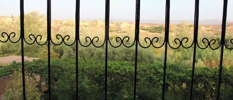 A view through ornate metal bars with greenery and distant buildings.