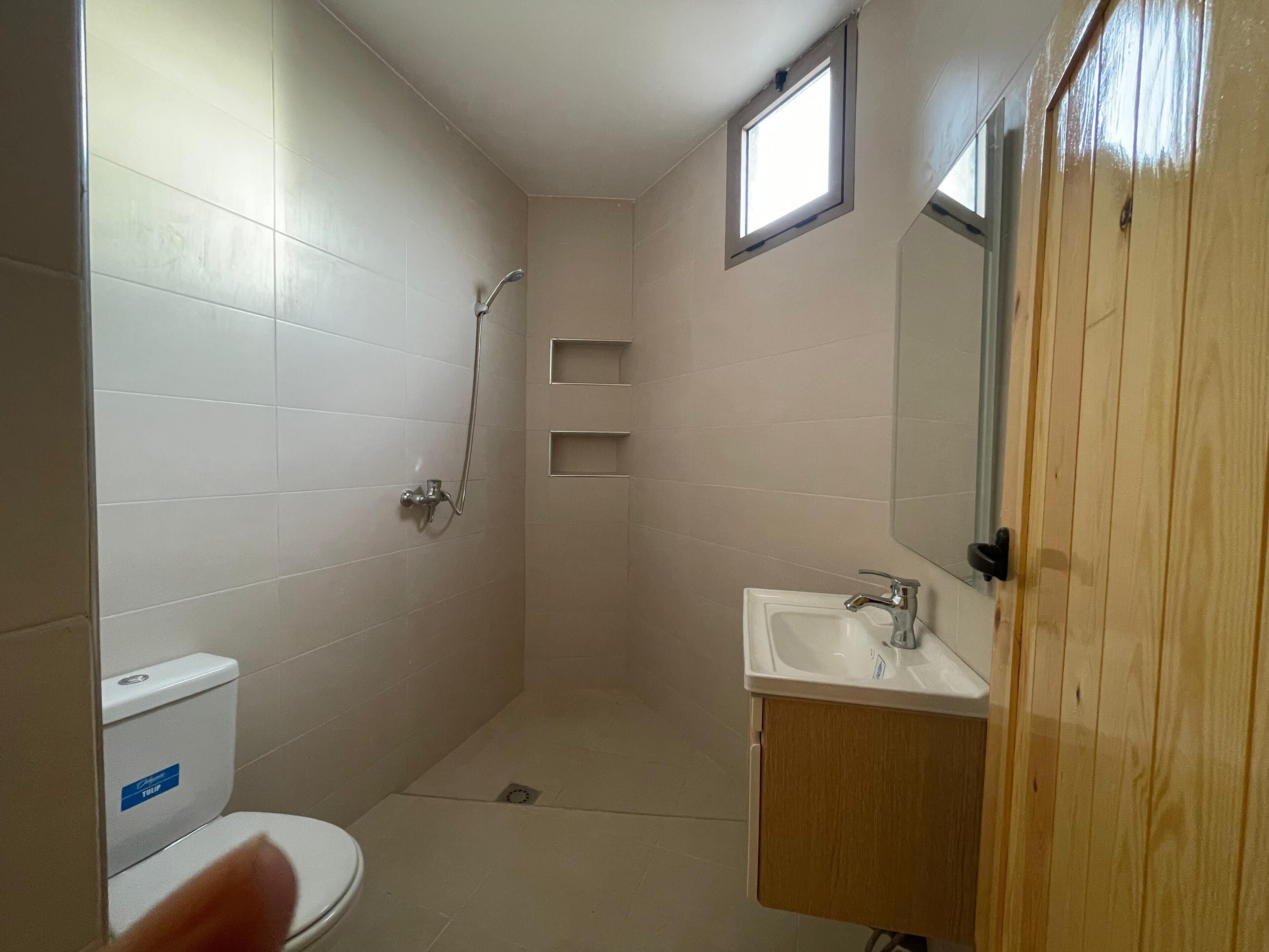 A small, narrow bathroom with a toilet, a shower, and a sink.