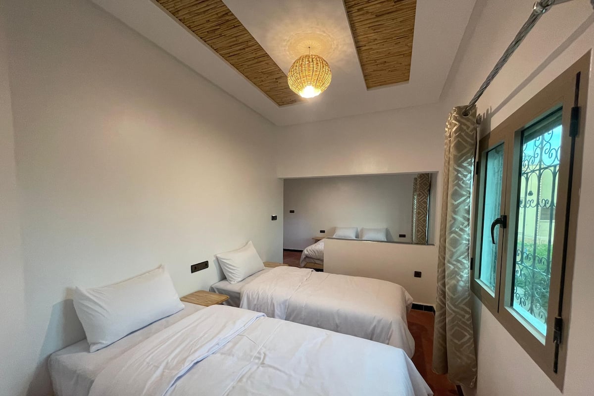 A hotel room with two beds, a large mirror, a ceiling light, and a window with a view.