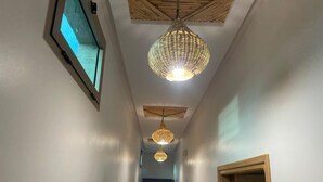 Un couloir avec un ventilateur de plafond, un luminaire en fibres tressées et une porte en bois.