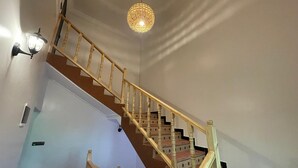 Un escalier avec des rampes en bois et un luminaire tressé suspendu au-dessus.